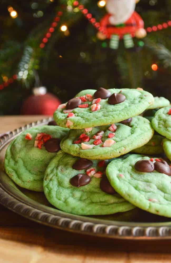 Minty green cookies with chocolate chips and peppermint chips piled up on a plate for Santa under the tree