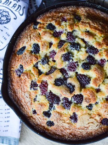 Overhead view of a skillet cake studded with blackberries baked and golden and ready to serve