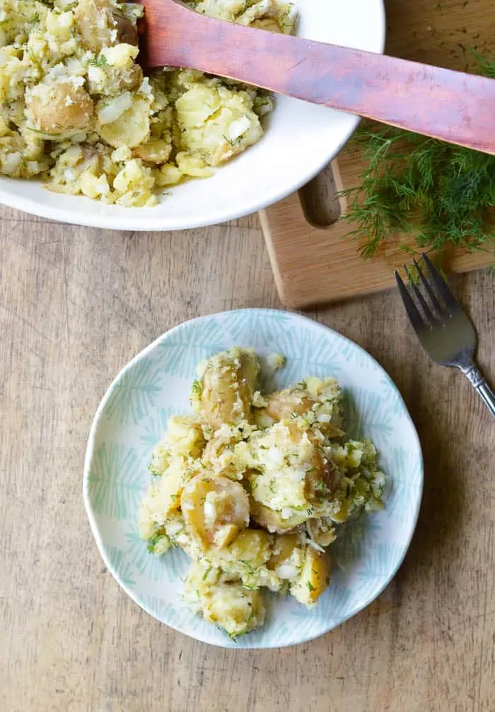 An overhead shot of Dill Potato Salad plated with the serving bowl and chopped fresh dill beside it.