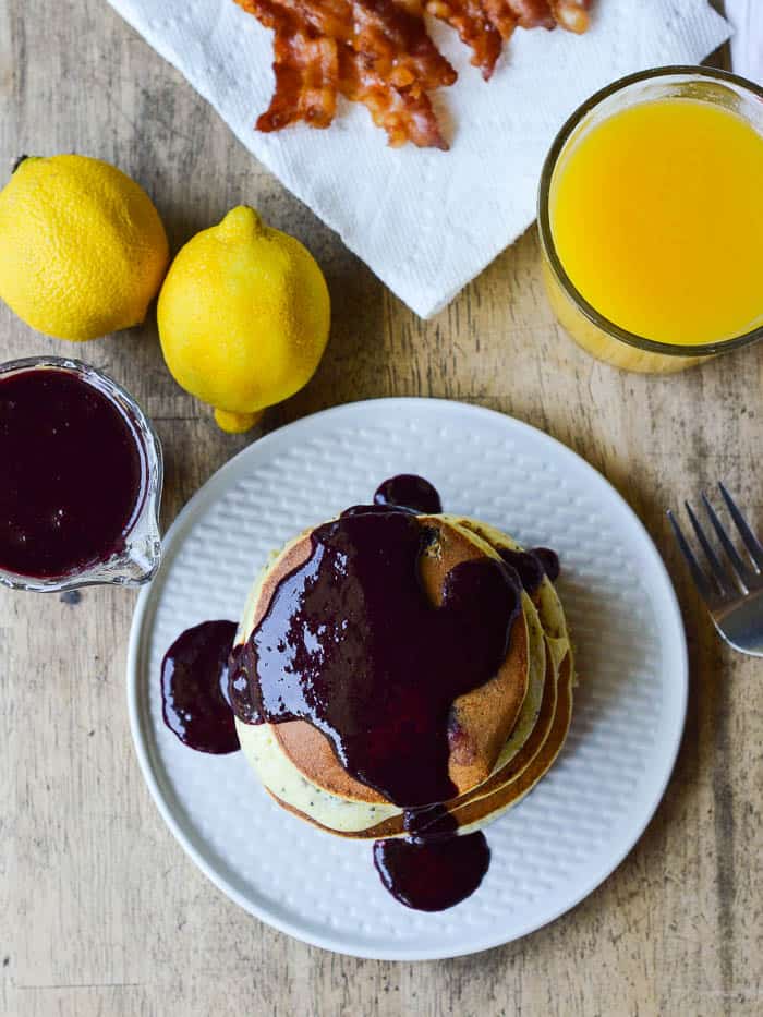 An overhead view of fluffy lemon poppy seed ricotta pancakes topped with blueberry syrup at the breakfast table.