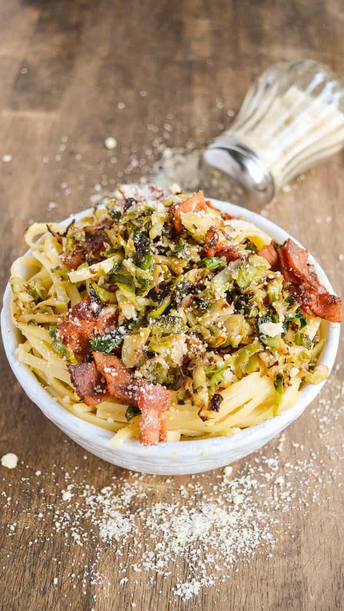 bowl of linguine carbonara with crispy Brussels sprouts and bacon, covered with grated Parmesan cheese