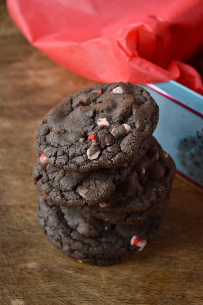 A stack of Hot Chocolate Peppermint Cookies next to a tissue paper lined cookie tin, ready to be packed up and shared