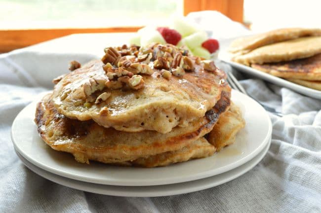 A landscape oriented photo of Banana Oat Pancakes stacked on white plates and drizzled with syrup.