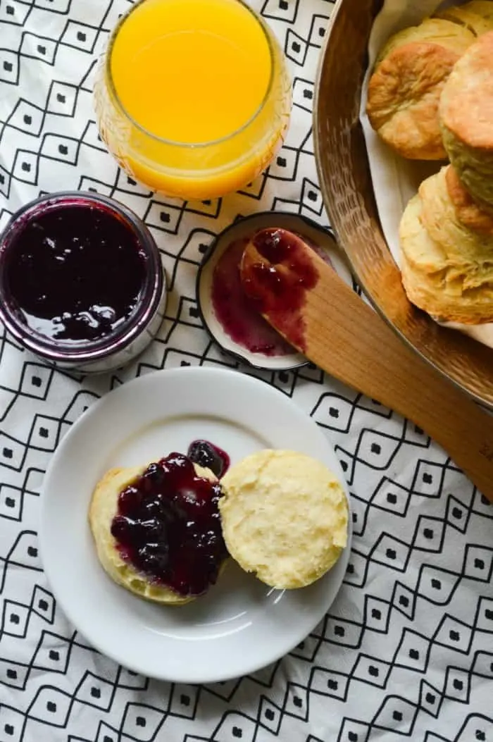 The Biggest Fattest Fluffiest All Butter Biscuits split on a plate and spread with blueberry lemon jam.