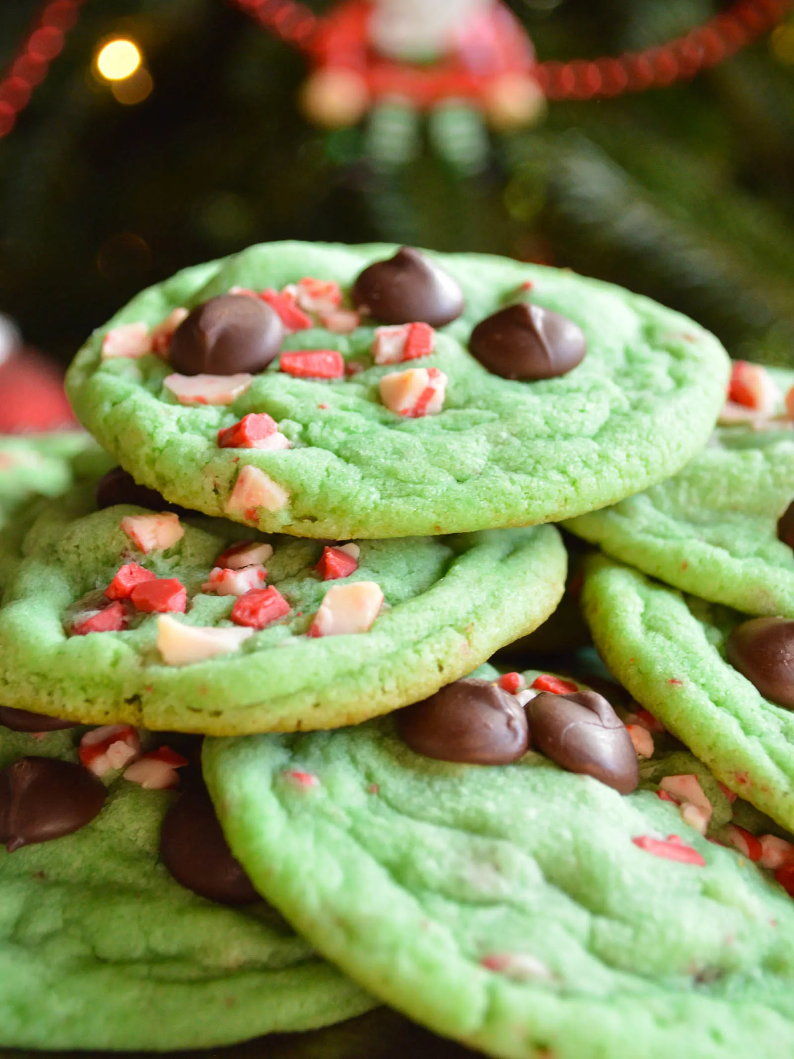 A pile of green chocolate chip "Grinch" cookies studded with chocolate chips aqnd peppermint chips