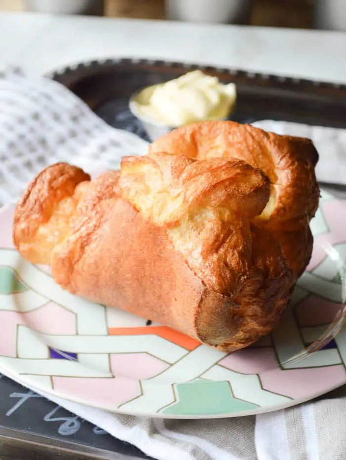A huge popover on a plate with soft butter on the side just waiting to be eaten