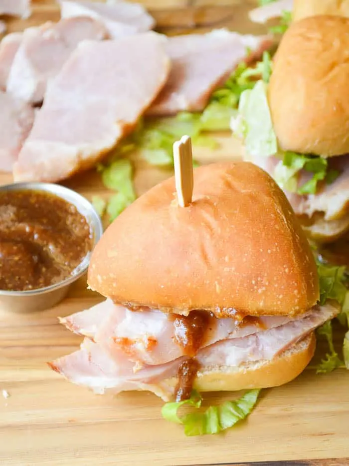 Close up of apple butter glazed ham piled on top of little 3-bite sandwiches oin a cutting board with more sliced ham