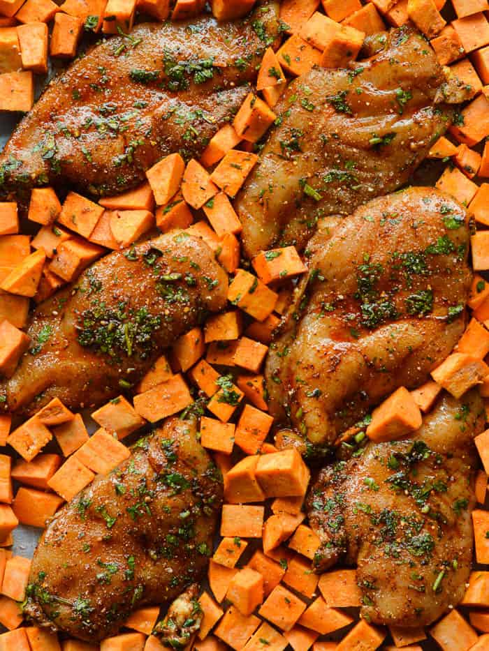 marinated cilantro chicken breasts and sweet potatoes spread out on a sheet pan ready for roasting