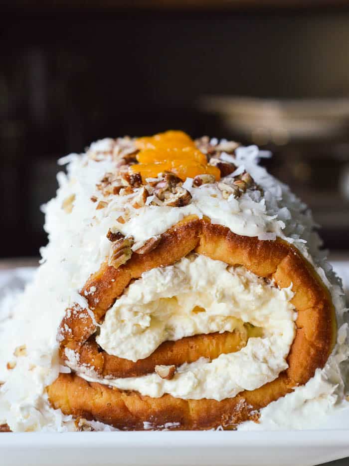 Pig Pickin Cake Roll is a twist on a mandarin orange cake with pineapple fluff frosting. It's filled, frosted, covered in coconut. and sprinkled with chopped pecans