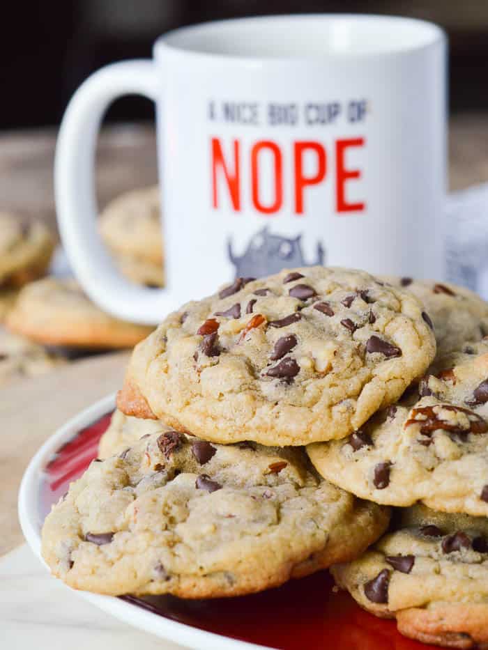 A pile of Chocolate Chip Blondie Cookies on a red plate with a funny coffee cup in the background