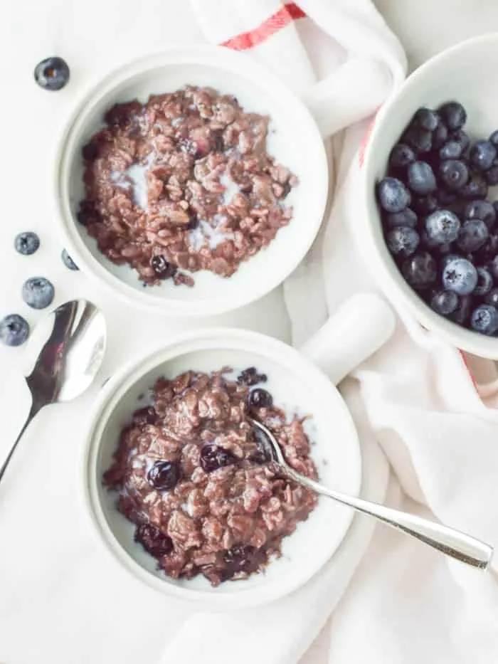 Overhead view of Blueberry Cinnamon Oatmeal in white crocks with a bowl of fresh blueberries.