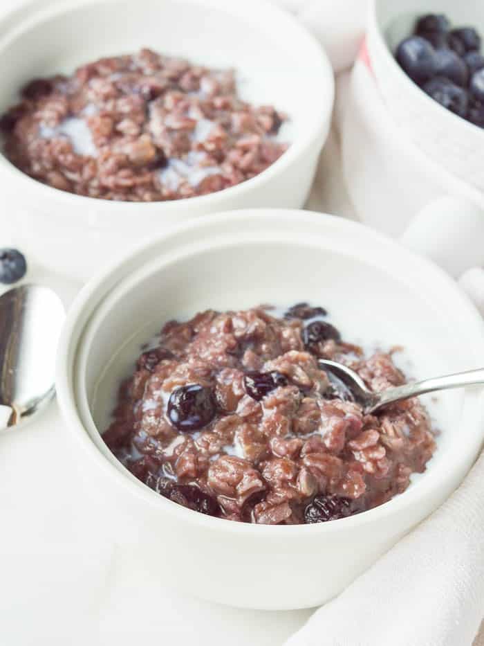 Bowl of Blueberry Cinnamon Oatmeal with a pretty purple hue and a splash of milk