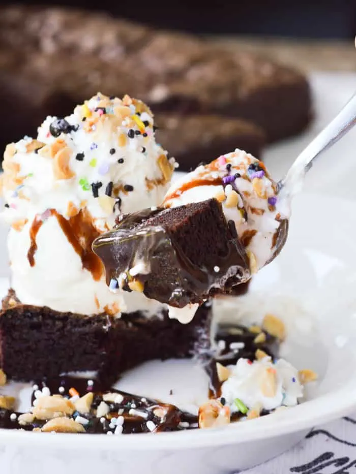 A decadent bite of homemade brownie sundae with vanilla ice cream and dripping with hot fudge
