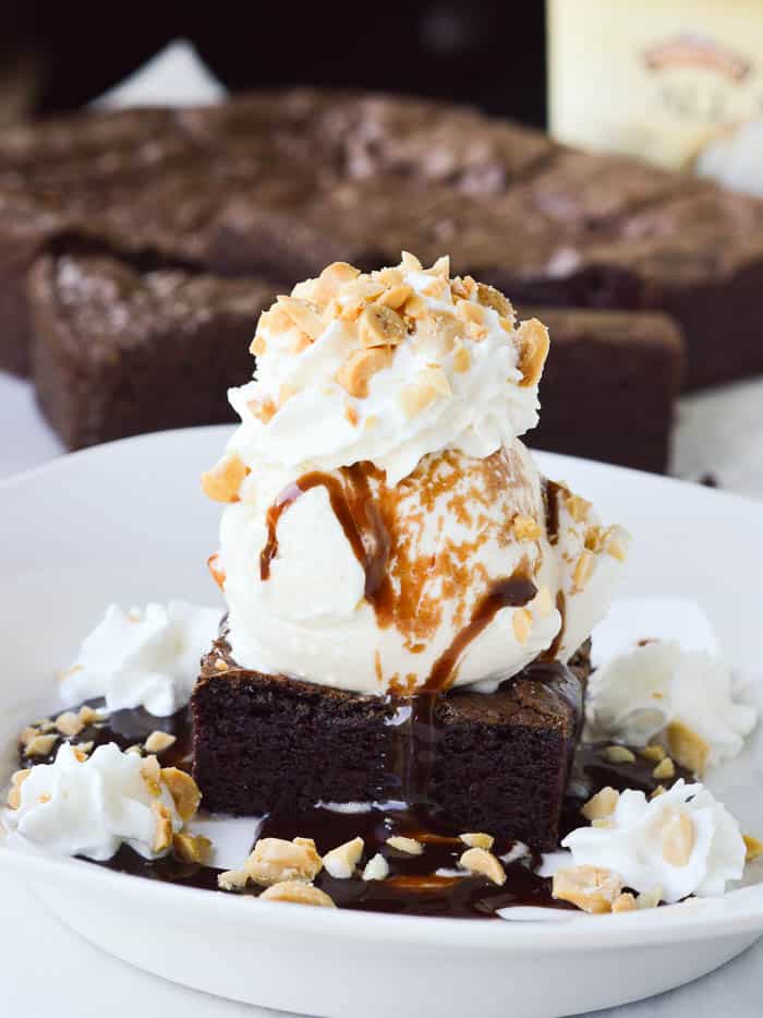 Homemade Brownie Sundae in a white dish with a pile of thick, fudgy homemade brownies in the background