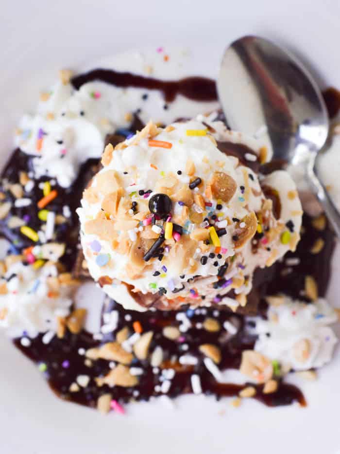 overhead view of a brownie sundae loaded up with hot fudge sauce, whipped cream, chopped peanuts, and sprinkles