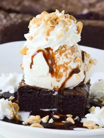 Square cropped image of the best homemade brownie sundae topped with hot fudge, whipped cream, and chopped peanuts