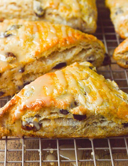 A square cropped close up image of golden brown run raisin scones, glazed and cooling on a cooling rack.