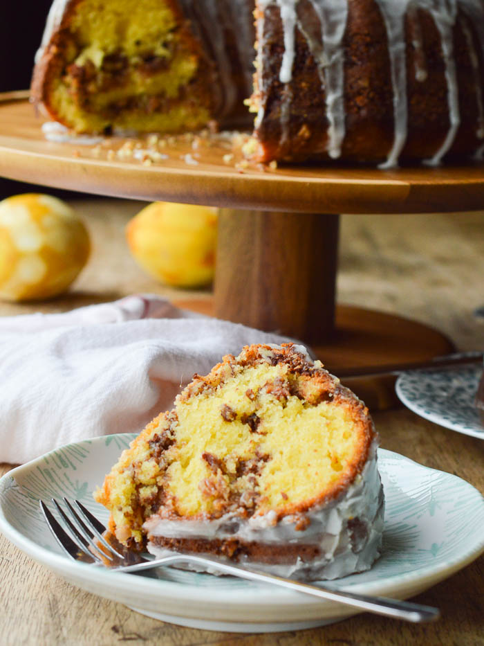 A slice of yellow bundt cake with ribbons of pecan streusel running through it. It's on a mint and white printed plate that has scalloped edges and there's a fork laying on the cake