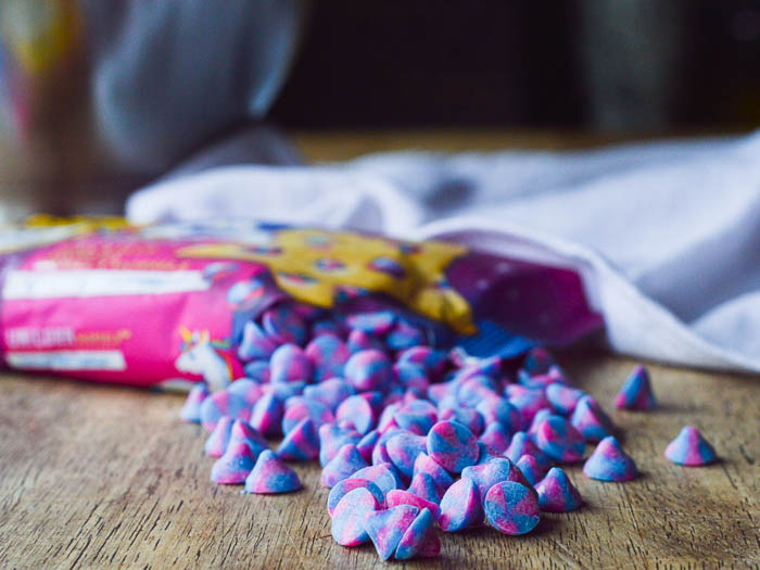An open bag of Nestle's Unicorn Baking Chips spilled out of the package and onto the table ready to measure out and bake with