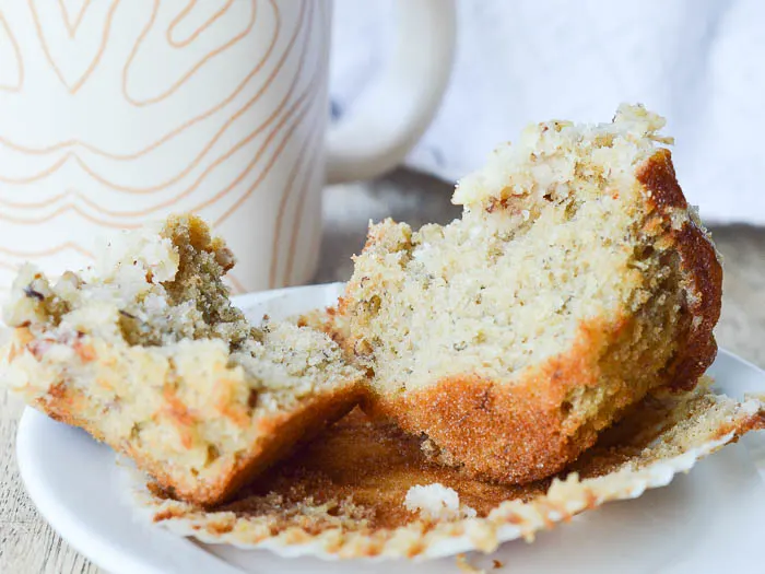 A banana muffin resting on its paper liner after its been split open to reveal all the flecks of banana baked in, and the moist, tender crumb. 