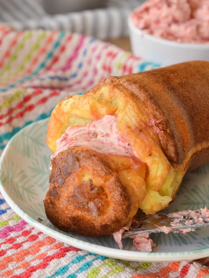 A split warm popover smeared with melty whipped strawberry butter. The butter has a pretty pink hue and you can tell the popover is warm because the butter is seeping into it. 