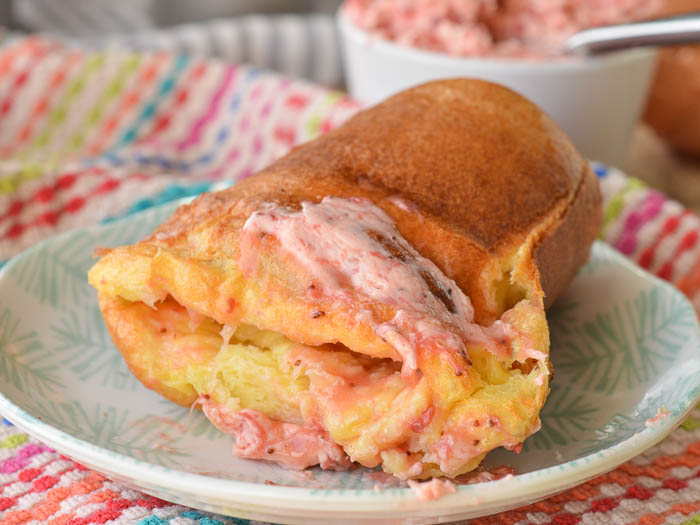 A split popover that's missing the top so that you can see the hollowed eggy inside smeared with pink melty strawberry butter with little flecks of strawberry seeds. 