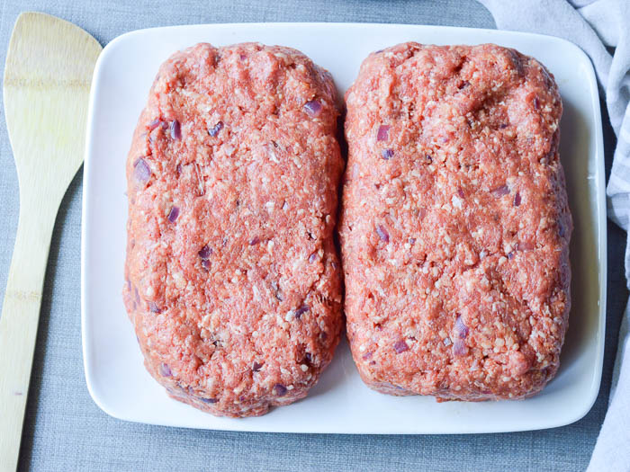 Two shaped loaves of meat on a plate ready to be grilled