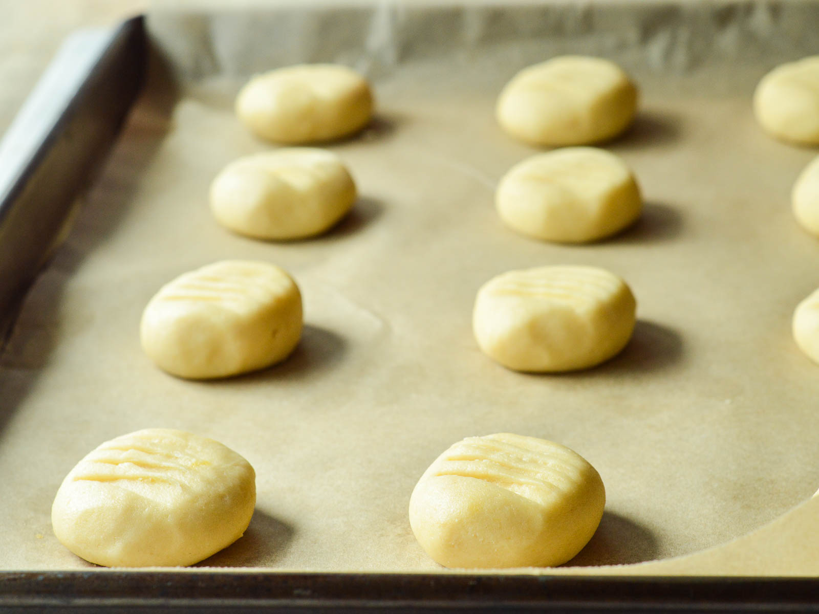 Soft balls of shortbread dough set 2" apart on a parchment lined baking sheet. Each unbaked cookie has been slightly pressed with a fork to make small ridges on top. 