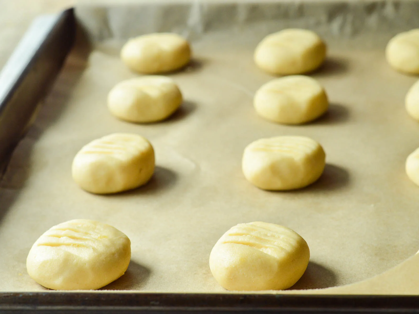 Soft balls of shortbread dough set 2" apart on a parchment lined baking sheet. Each unbaked cookie has been slightly pressed with a fork to make small ridges on top.