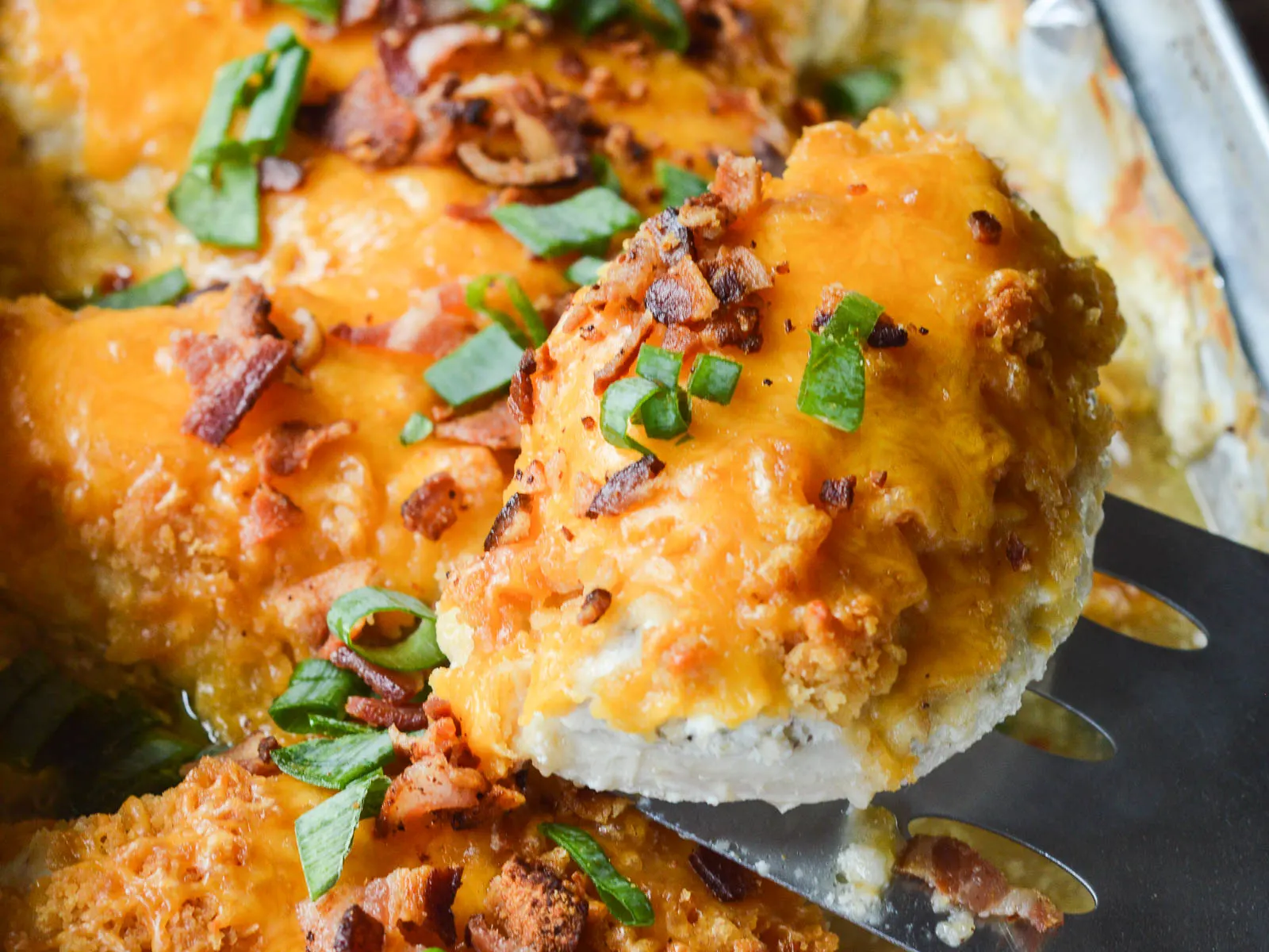 Baked Smothered Cheesy Sour Cream Chicken on a metal spatula being lifted from the hot foil-lined baking pan