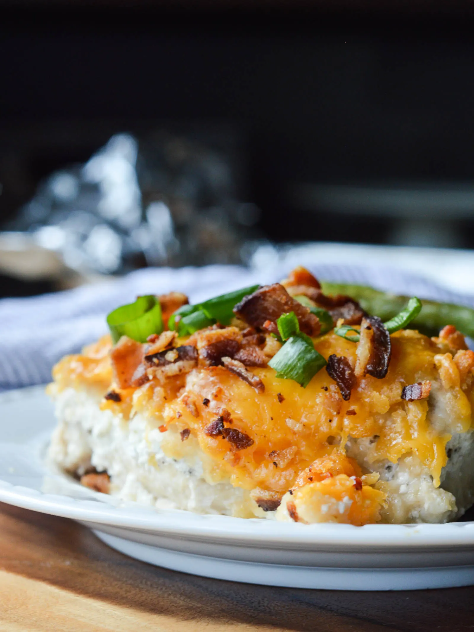 A dinner plate piled with baked chicken breast smothered in seasoned sour cream, melty cheddar cheese, chopped bacon, and chopped green onions