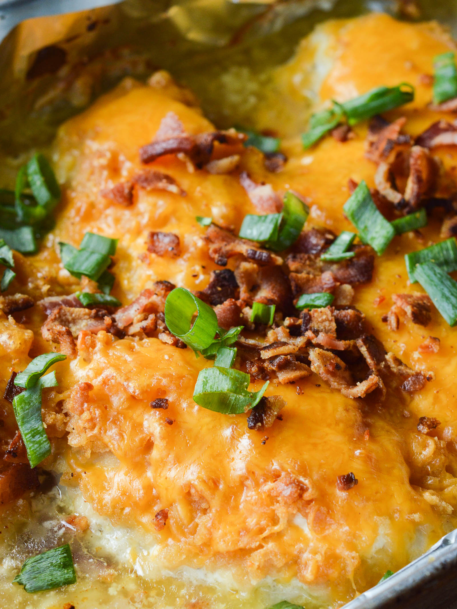 Baked chicken breasts in a foil-lined pan smothered in cheese, bacon, and green onions. 