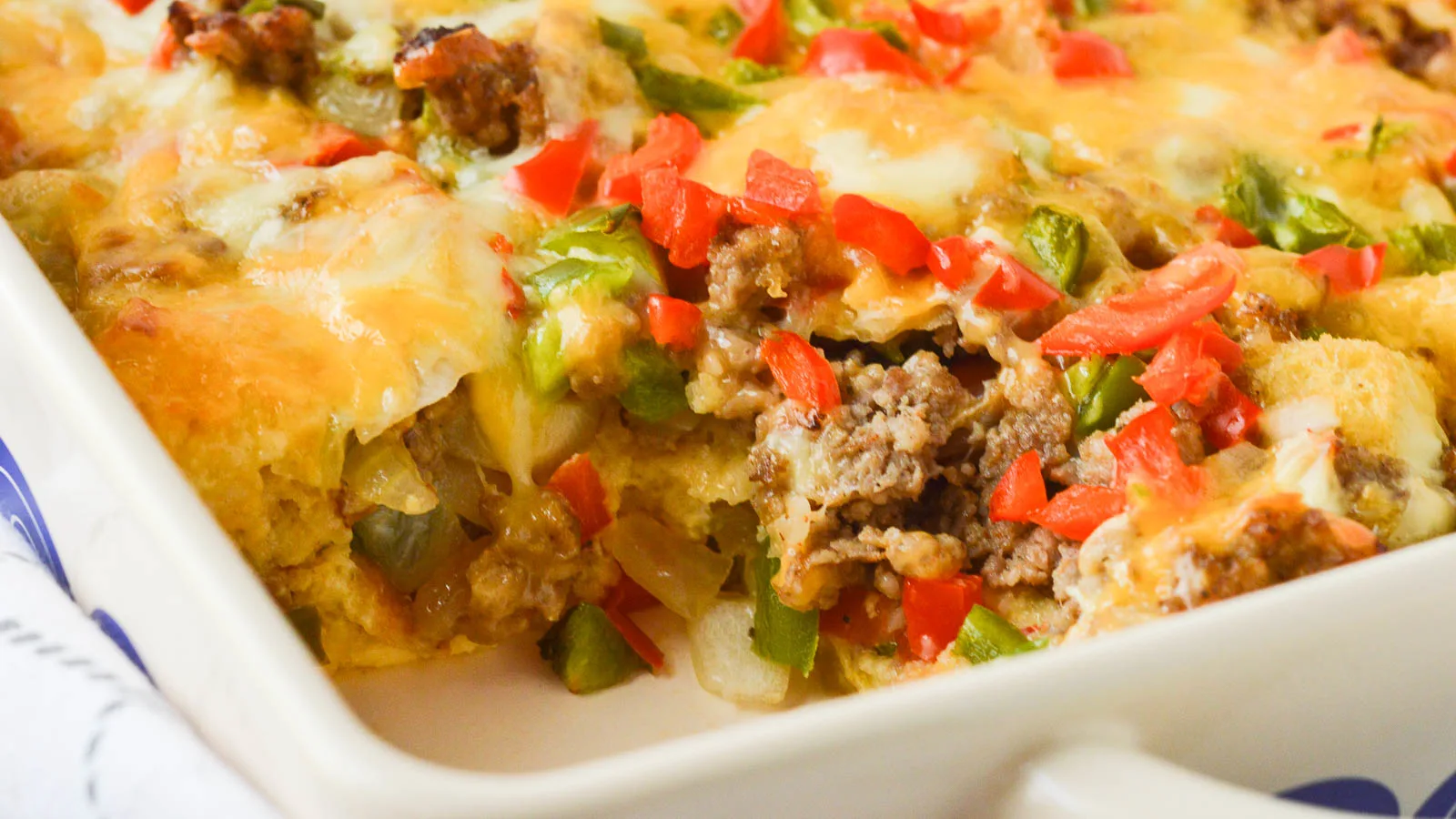 A close up image of a sausage strata, sliced, so that you can see the crumbled, cooked sausage, onions, peppers, and cheese spilling out into the empty space of the casserole dish