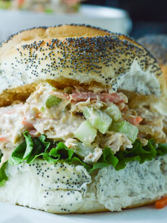 Buffalo Chicken Salad piled onto a fluffy poppy seed roll with leafy lettuce.