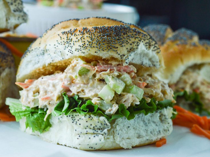 Buffalo Chicken Salad piled onto a fluffy poppy seed roll with leafy lettuce.