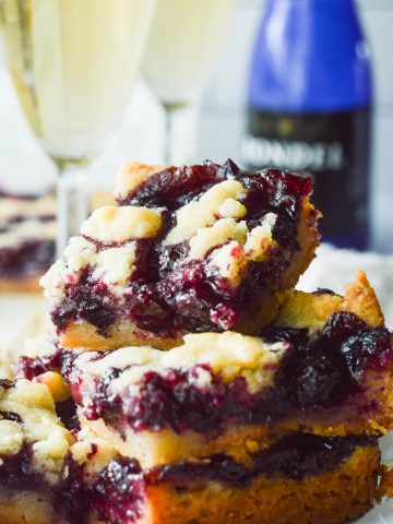 A stack of Blueberry Crumble Bars with several poured glassed of champagne in the background.