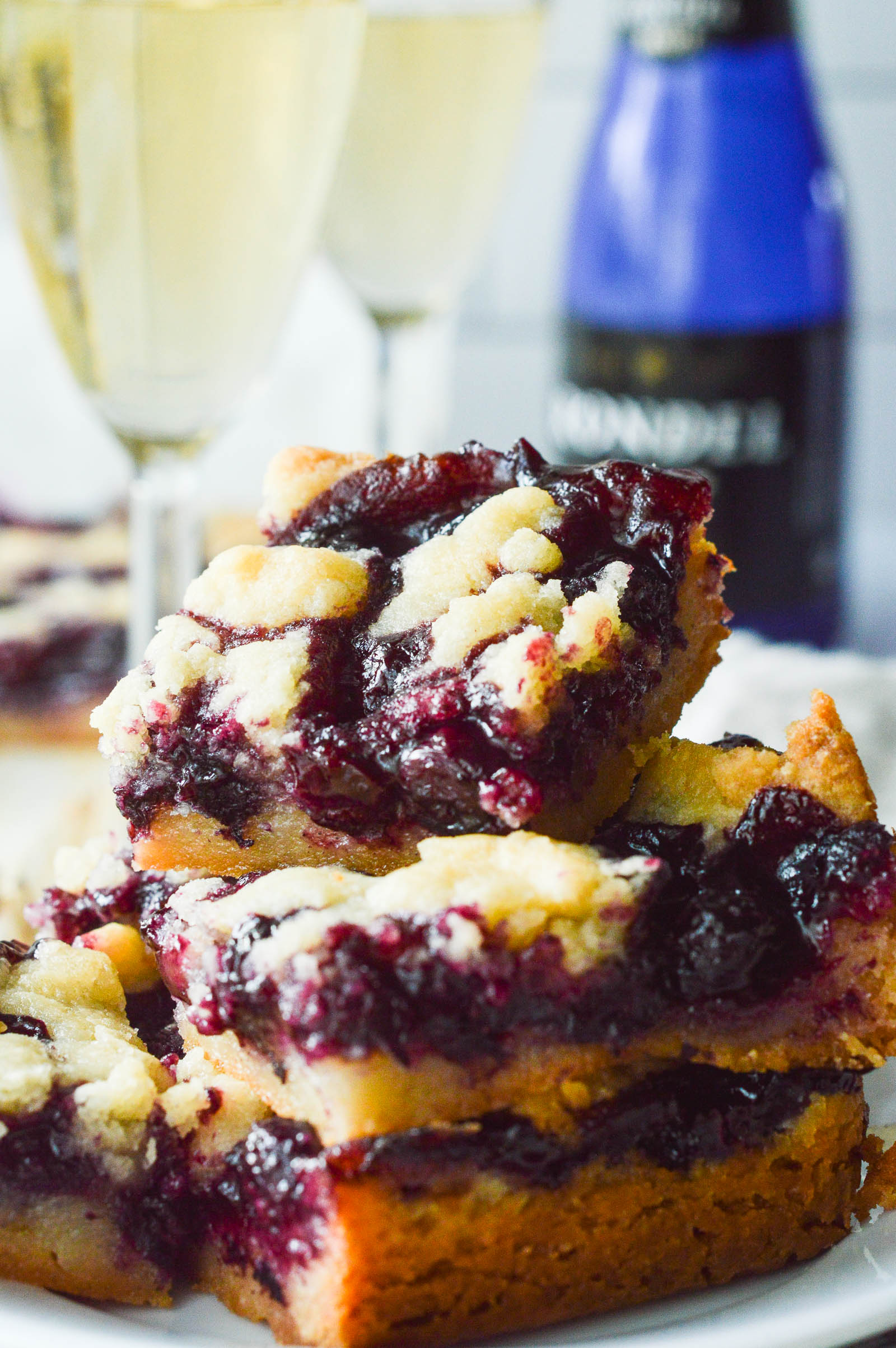 A stack of Blueberry Crumble Bars with several poured glassed of champagne in the background.