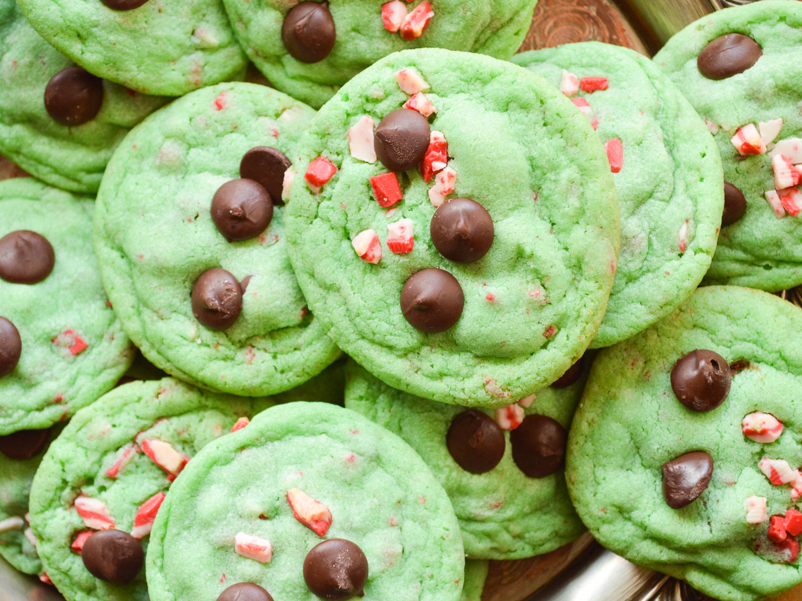 The best Grinch Cookies all piled up on a wooden serving board. they are green and studded with chocolate chips