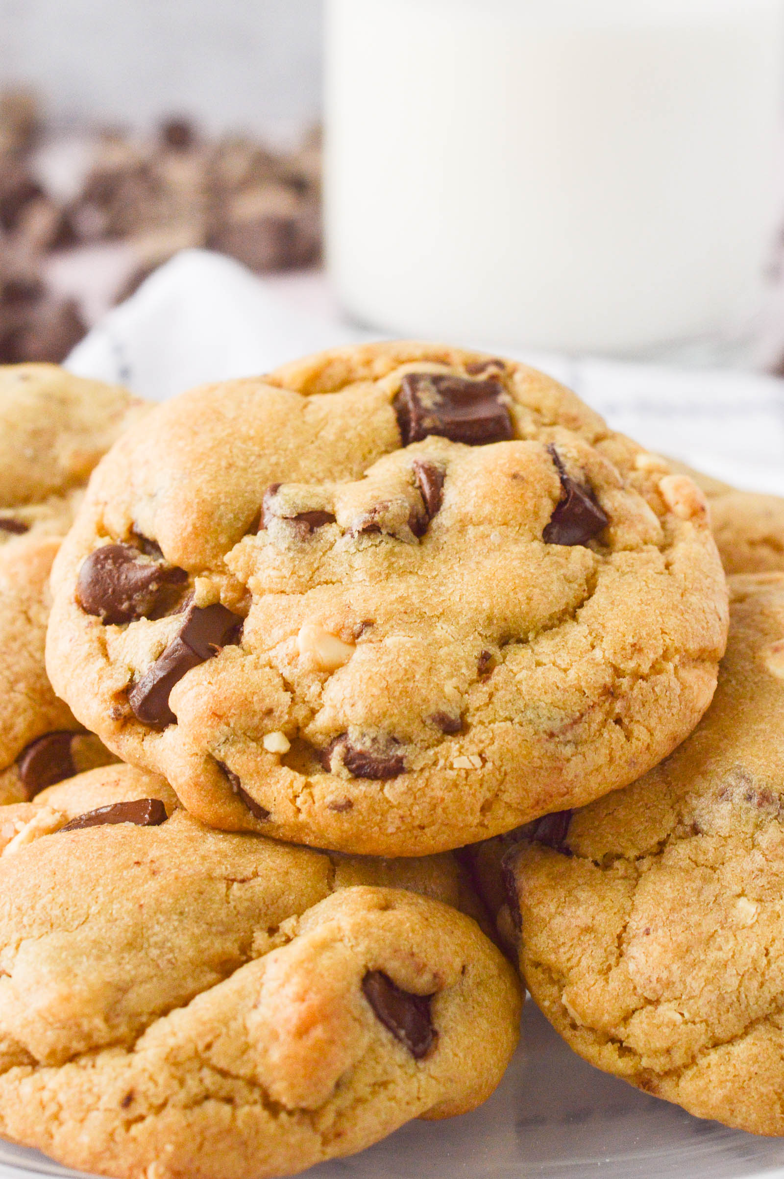 A close up of a chocolate chip cookie made with a brown sugar base flecked with coarse salt. Glass of milk in the background