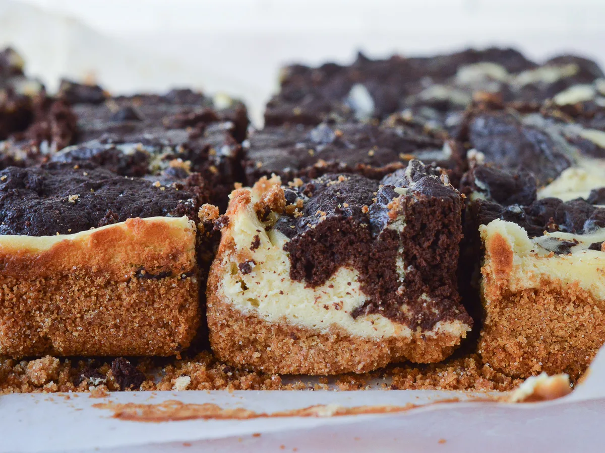 A close up of Cheesecake Brownie Bars with Graham Cracker Crust. You can see the buttery graham cracker layer on the bottom, and the swirled brownies + cheesecake in decadent detail. 