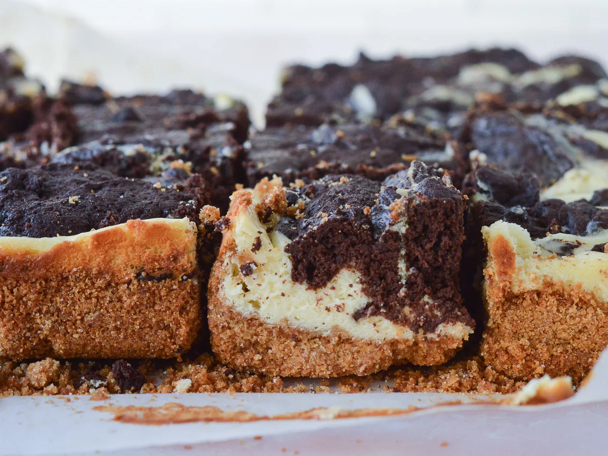A close up of Cheesecake Brownie Bars with Graham Cracker Crust. You can see the buttery graham cracker layer on the bottom, and the swirled brownies + cheesecake in decadent detail.