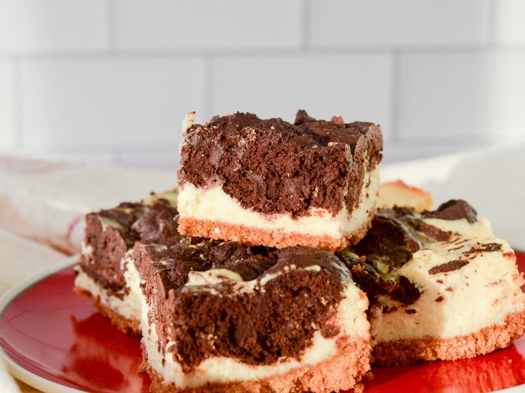 Lancape oriented image of Cheesecake Brownie Bars with a graham cracker crust stacked on a red plate
