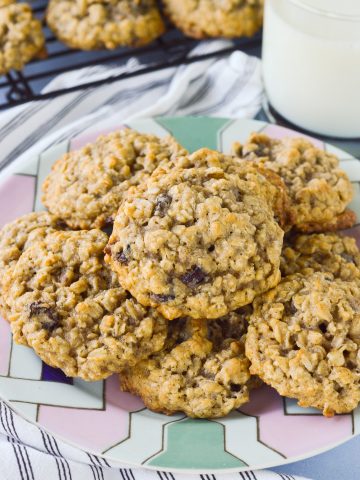 A plate piled high with thick oatmeal raisin cookies, with a glass of milk nearby.