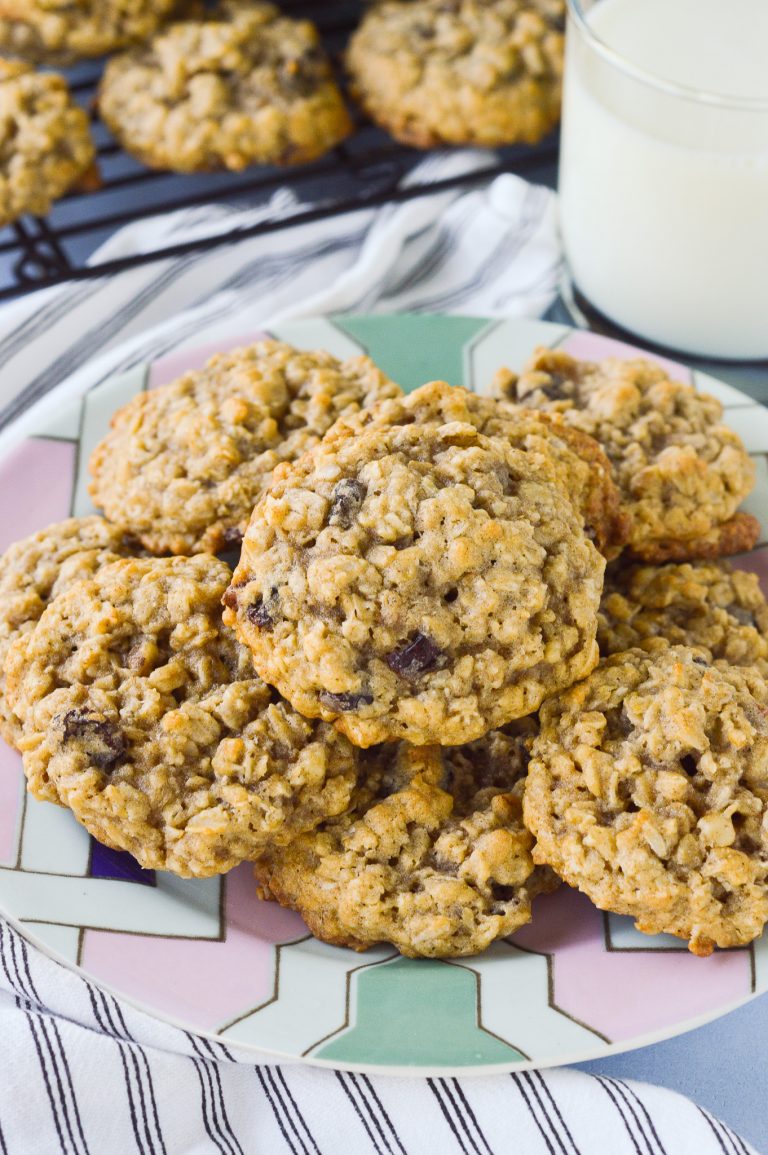 A plate piled high with thick oatmeal raisin cookies, with a glass of milk nearby.