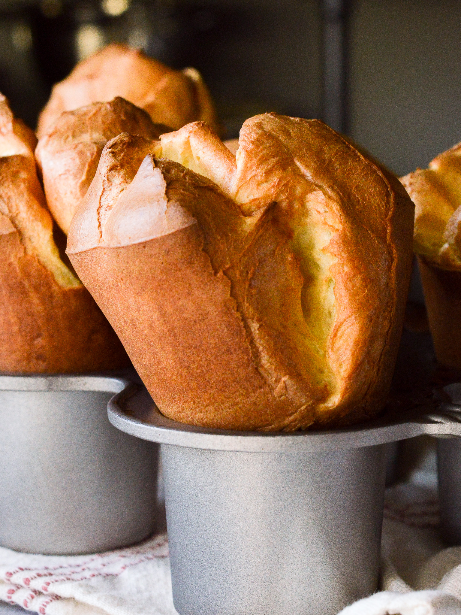 Close up of tall golden brown popovers bursting from the pan after baking. 