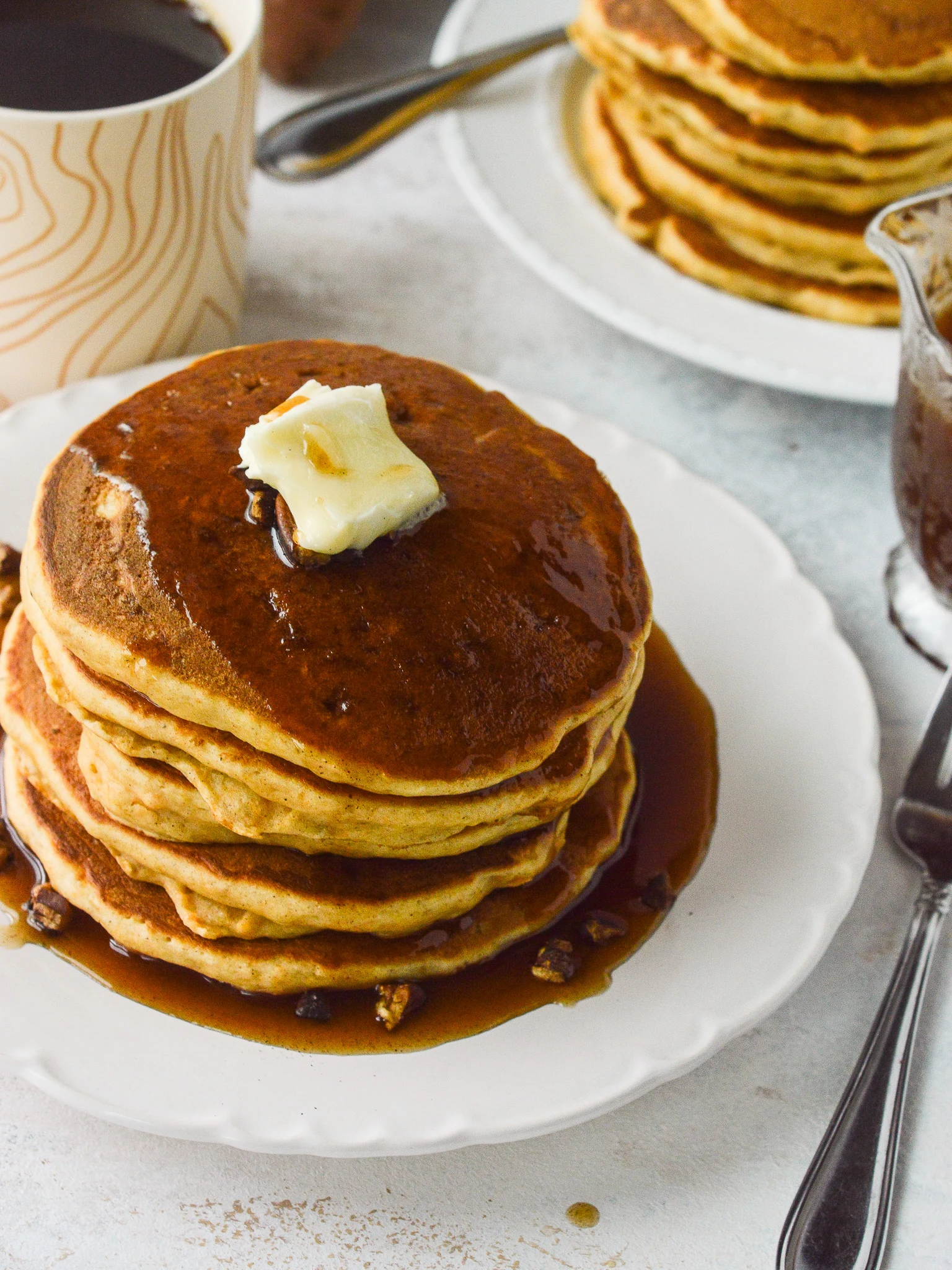 Table set for two with coffee, two stacks of pancakes, and a carafe of syrup. 