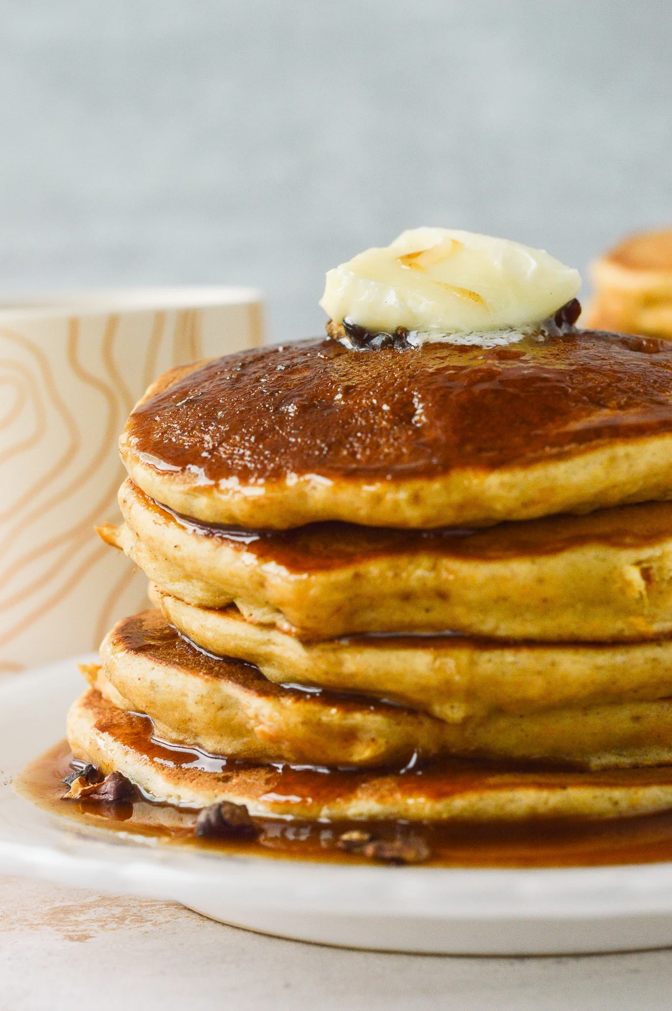 A stack of golden sweet potato pancakes topped with cinnamon syrup, a pat of butter, and toasted walnuts.
